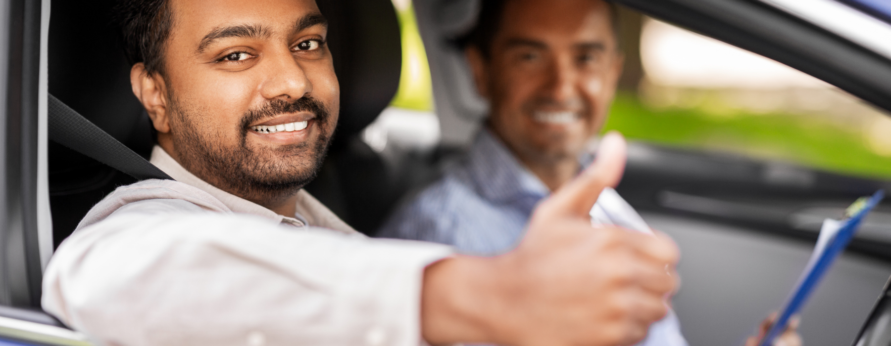 Smiling learner driver giving thumbs up next to a driving instructor inside a car during a lesson